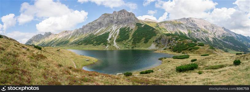 Mountain landscape: Rocky mountain range, clear water lake and blue cloudy sky; Panorama