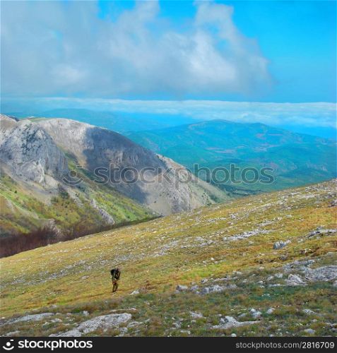 Mountain landscape with clouds and blue sky. Hiker climbing up the hill.