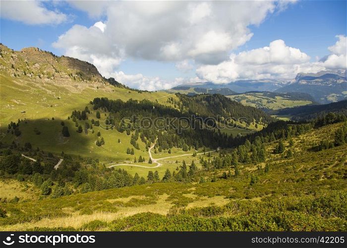 Mountain landscape with valley, trails, green fields and blue sky with clouds