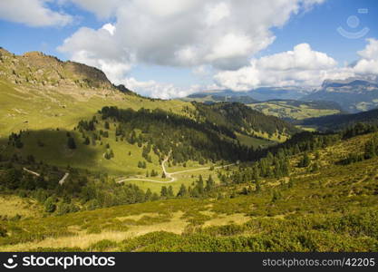 Mountain landscape with valley, trails, green fields and blue sky with clouds