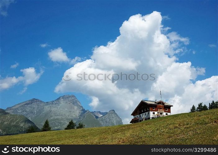 Mountain lodge in italian alps; in background a rocky peak, cloudy sky; summer season.