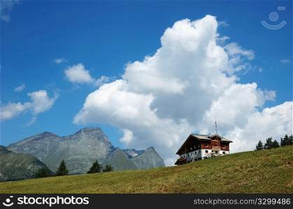 Mountain lodge in italian alps; in background a rocky peak, cloudy sky; summer season.