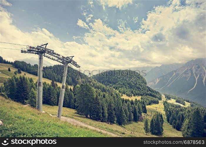 Mountain panorama with forest, Dolomites, valley and chairlift in summer. Sky with clouds. Photos with vintage effect filter.