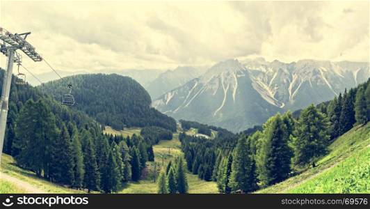 Mountain panorama with forest, Dolomites, valley and chairlift in summer. Sky with clouds. Photos with vintage effect filter.