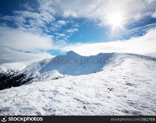 Mountain peak in the snow under the bright sun. Winter landscape. The concept of travel and privacy. Mountain peak in the snow under the bright sun