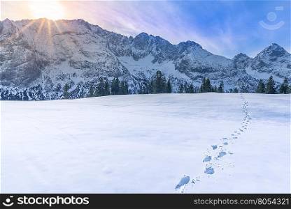 Mountain peaks in winter - Sunny, alpine landscape with the peaks of the Austrian Alps mountains on the horizon and a thick blanket of snow in the foreground, with footprints on it.
