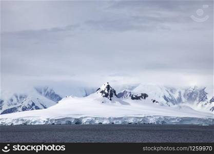 Mountain peaks of mountains covered with ice and snow protrude through cloud cover in Antarctica