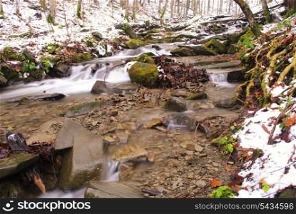 Mountain river is running down in forest under snow. Wild nature