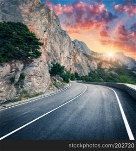 Mountain road and beautiful sky at sunset. Colorful landscape with high rocks, winding asphalt road, trees and blue sky with red and orange clouds in summer. Travel. Scenery with roadway in mountains
