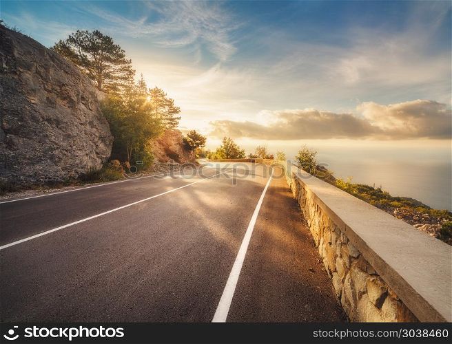 Mountain road at sunset in Europe. Landscape with rocks, sunny sky with clouds and beautiful asphalt road in the evening in summer. Colorful travel background. Highway in mountains. Transportation. Mountain asphalt road at sunset in summer in Europe