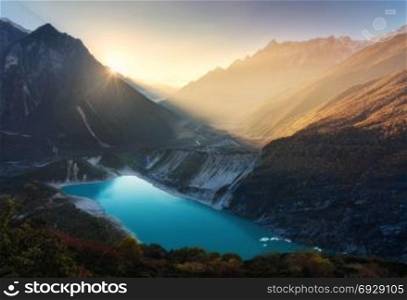 Mountain valley and lake with turquoise water at sunrise in Nepal. Majestical landscape with high mountains, lake, lightened hills, rocks, sun with yellow light and sky. Bright sunny morning. Travel