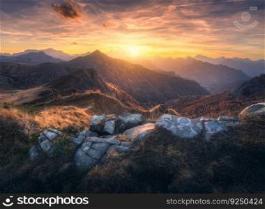 Mountain valley at colorful sunset in autumn in Dolomites, Italy. Colorful landscape with rocks, stones, mountain ridges, hills, orange grass and forest, golden sky with clouds in fall. Hiking. Nature