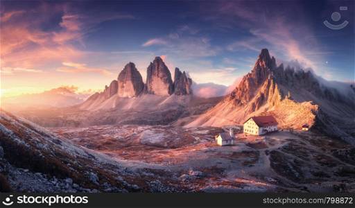 Mountain valley with beautiful house and church at sunset in autumn. Landscape with buildings, high rocks, colorful sky, clouds, sunlight. Mountains in Tre Cime park in Dolomites, Italy. Italian alps. Mountain valley with beautiful house and church at sunset