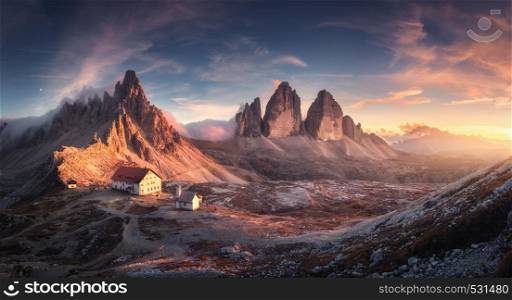 Mountain valley with beautiful house and church at sunset in spring. Landscape with buildings, high rocks, colorful sky, clouds, sunlight. Mountains in Tre Cime park in Dolomites, Italy. Italian alps