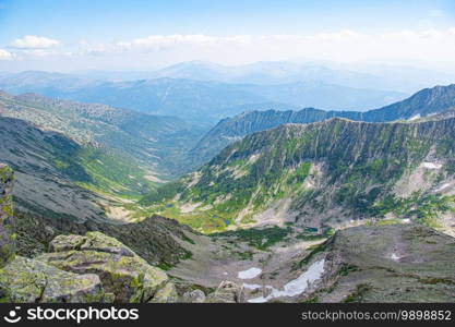 Mountain valley with stone ridge and trees on horizon. Travel through wild rocks in summer. Mountain landscape against blue sky on sunny day