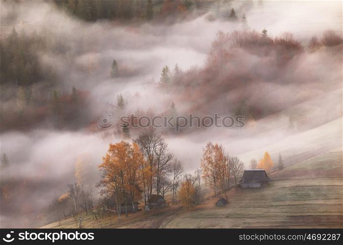 Mountain village in clouds of fog and smoke in the autumn morning. Farm on hills in the mountains. Waves of mist in a forest.