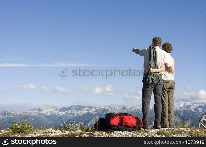 Mountaineer couple with rope and rucksacks standing on a mountain summit