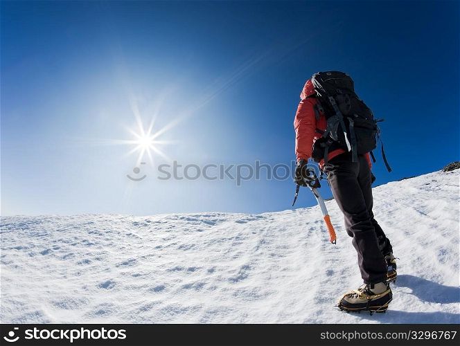 Mountaineer reaching the top of a snowcapped mountain peak. Horizontal frame.
