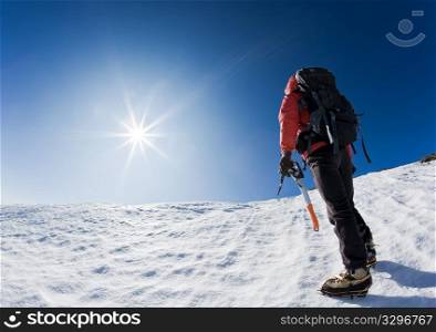 Mountaineer reaching the top of a snowcapped mountain peak. Horizontal frame.