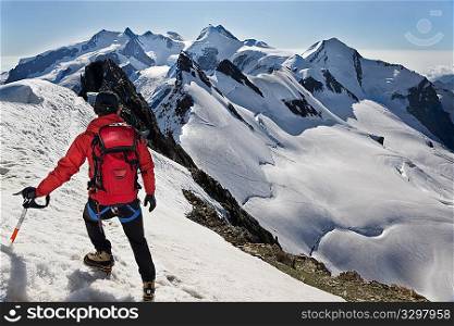 Mountaineer walks down along the snowy ridge of Breithorn, exactly on the swiss-italian border. IIn background the main peaks of Monte Rosa massif (4650 mt, the second highest point in continental Europe) Switzerland, Europe.