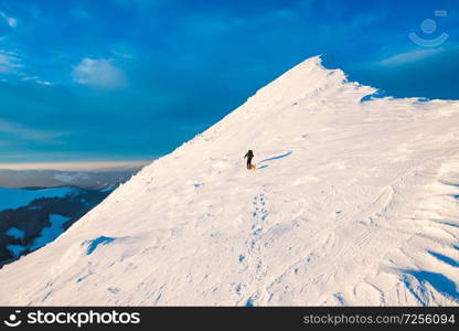 Mountaineer with dog climbing on a slope at snowy mountain top in sunset evening