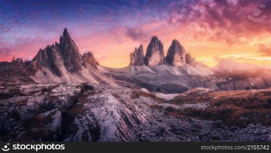 Mountains and beautiful sky with colorful clouds at sunset. Summer landscape with mountain peaks, stones, grass, trails, violet sky with red clouds. High rocks. Tre Cime in Dolomites, Italy. Nature