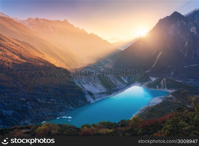 Mountains and lake with blue water at sunset in Nepal. Majestic landscape with high mountains, lake, lightened hills, rocks, yellow sunlight and blue sky. Bright sunny evening. Travel. Nature