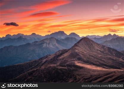 Mountains at beautiful sunset in autumn in Dolomites, Italy. Landscape with rocks, forest on hills and orange sky with red clouds in the evening. Autumn scenery with mountain valley. Italian alps