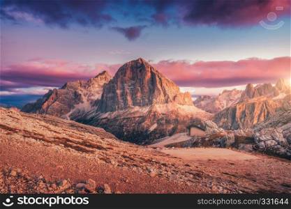 Mountains at sunset in Dolomites, Italy. Landscape with high rocks, stony trail, small house, blue sky with pink clouds in the evening. Autumn scenery with mountain valley. Italian alps at dusk