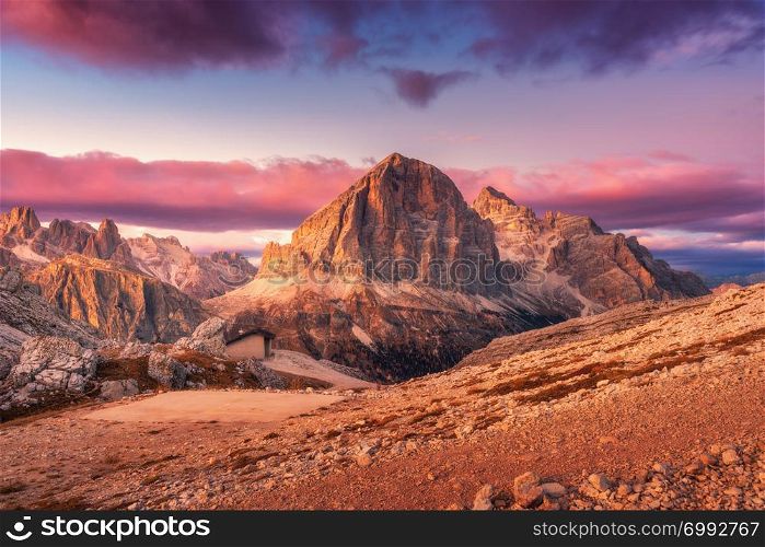 Mountains at sunset in Dolomites, Italy. Landscape with high rocks, stony trail, small house, purple sky with pink clouds in the evening. Autumn scenery with mountain valley. Italian alps at dusk