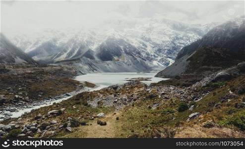 Mountains, lakes and meadow landscape in cold climate country with snow and cloudy weather on the mountains. The landscape was shot in Mt Cook, New Zealand, famous place for trekking and outdoors.