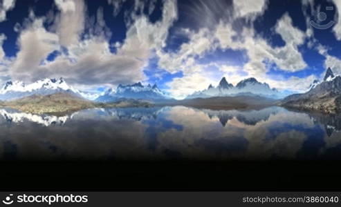 Mountains on the horizon. Their tops in the snow. Above them, the vast sky and slowly floating clouds. All this is reflected in the water of a mountain lake. Footage made &#8203;&#8203;in the form of a panorama.