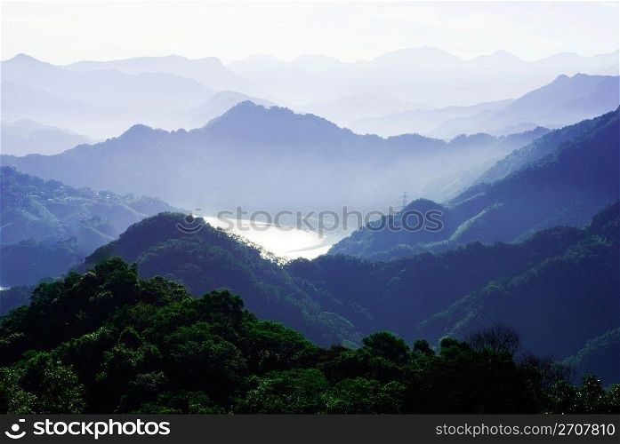mountains surround lake with light fog. The lake surface reflect sunshine.