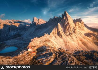 Mountains with beautiful house and church at sunset in autumn. Landscape with buildings, high rocks, lake and blue sky with moon and clouds at dusk. Aerial view of Tre Cime park in Dolomites, Italy