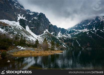 Mountains with snow and small waterfalls flowing to a lake with stormy weather