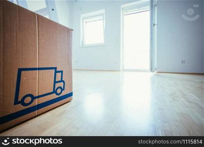 Move. Cardboard box in a clean and bright room with wooden floor. Moving into a new home.