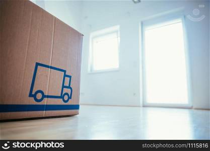 Move. Cardboard box in a clean and bright room with wooden floor. Moving into a new home.