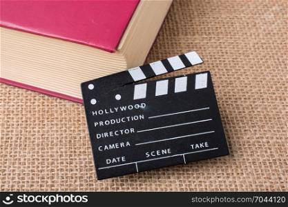 Movie clapper beside a book on a canvas background