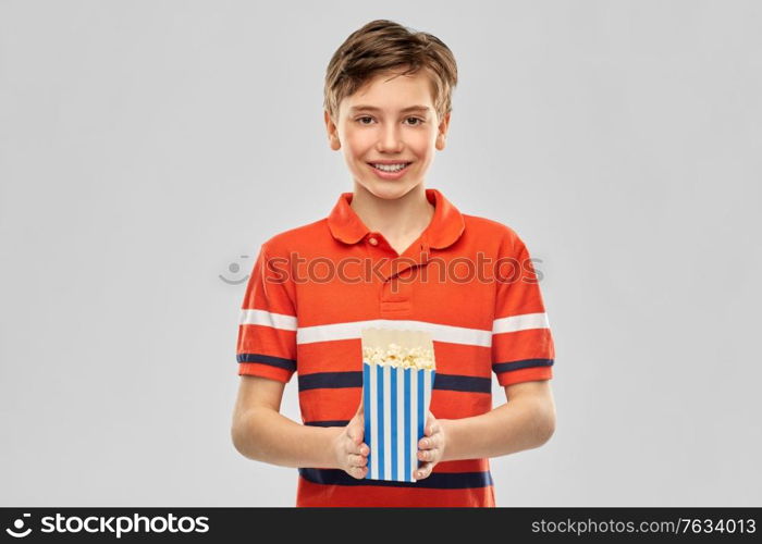 movie theater, cinema and people concept - portrait of happy smiling boy eating popcorn from striped bucket over grey background. smiling boy eating popcorn