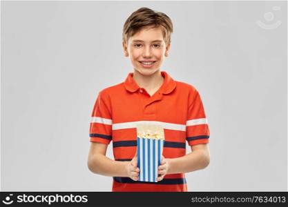 movie theater, cinema and people concept - portrait of happy smiling boy eating popcorn from striped bucket over grey background. smiling boy eating popcorn