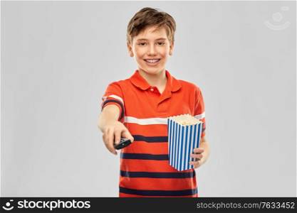 movie theater, cinema and television concept - portrait of happy smiling boy with popcorn and tv remote control over grey background. smiling boy with popcorn and tv remote control