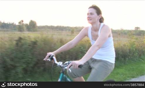 Moving alongside a young woman riding a bike on a paved prairie path with the sunset behind her.
