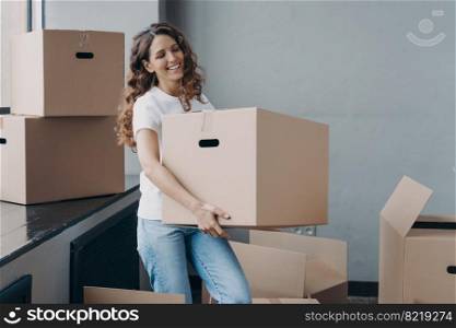 Moving day. Happy female tenant homeowner carrying cardboard box with household things. Smiling girl enjoying preparations to relocation to new house, packing belongings. Removal and delivery service.. Moving to new house. Happy female tenant homeowner carrying cardboard box with things for relocation