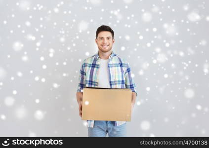 moving, delivery, housing, accommodation and people concept - smiling young man with cardboard box at home over snow