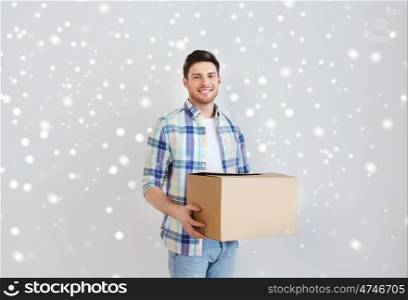 moving, delivery, housing, accommodation and people concept - smiling young man with cardboard box at home over snow
