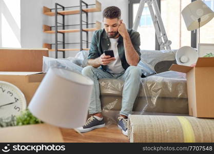 moving, eviction and real estate concept - sad man with smartphone and boxes at new home. sad man with smartphone and boxes moving home