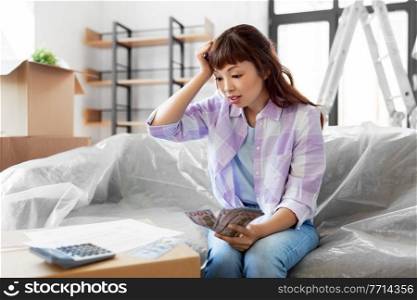 moving, finances and real estate concept - asian woman with money, bills and calculator at new home having financial problems. asian woman moving to new home and counting money