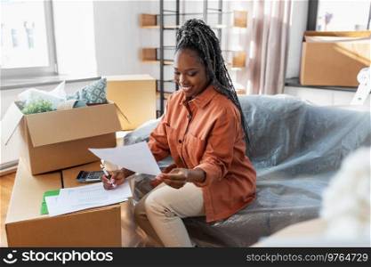 moving, finances and real estate concept - happy smiling woman with bills and calculator at new home. woman with bills and calculator moving to new home