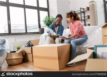 moving, finances and real estate concept - happy smiling women with money, bills and calculator at new home. women moving to new home and counting money