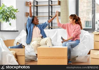 moving, finances and real estate concept - happy women with money, bills and calculator at new home making high five gesture. happy women moving to new home and counting money